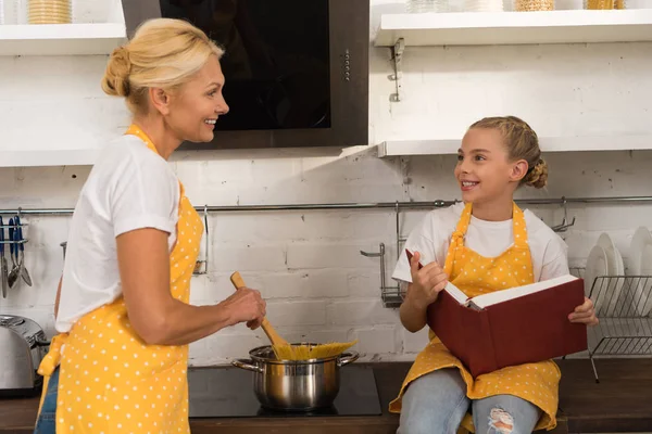 Gelukkig Grootmoeder Spaghetti Koken Kijken Glimlachend Kleindochter Bedrijf Kookboek Keuken — Stockfoto