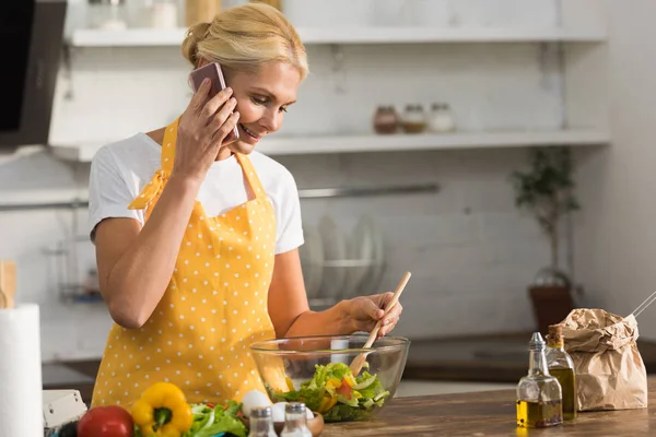 Sonriente Mujer Madura Delantal Hablando Por Teléfono Inteligente Mientras Cocina —  Fotos de Stock