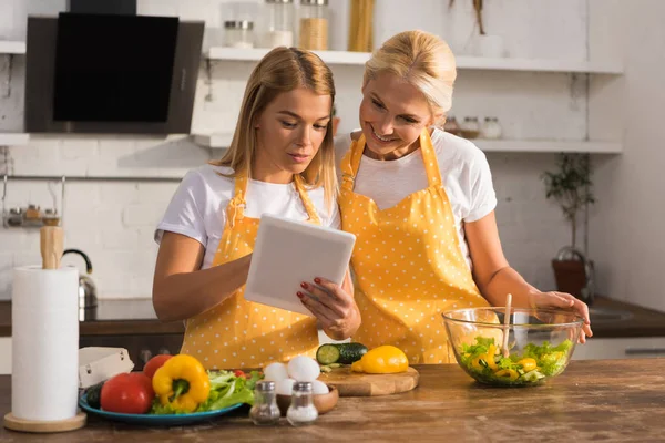 Yetişkin Anne Kızı Birlikte Pişirme Sırasında Dijital Tablet Kullanarak Önlük — Stok fotoğraf