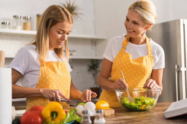 幸せの熟女と若い娘のキッチンで一緒に野菜サラダを調理 — ストック写真