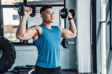 Genç Asyalı sporcu spor salonunda dumbbells ile egzersiz konsantre