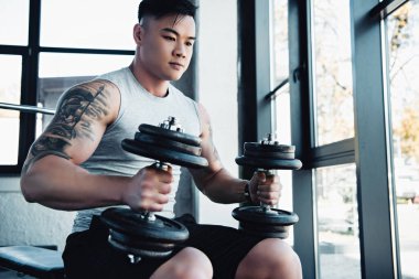 Genç Asyalı sporcu spor salonunda dumbbells ile egzersiz konsantre