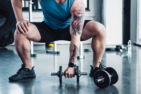 partial view of young sportsman exercising with dumbbells in gym