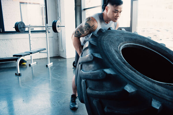 focused young sportsman flipping heavy tire at gym