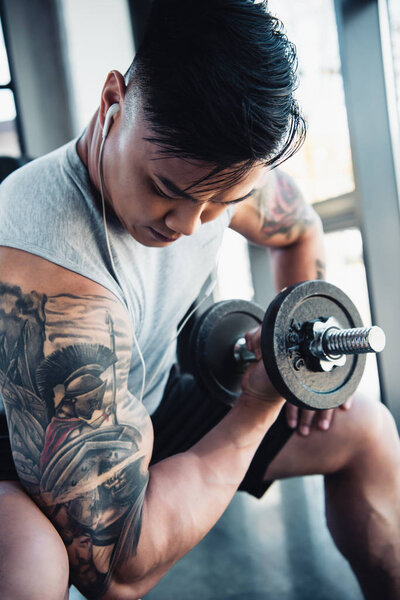 concentrated young sportsman exercising with dumbbell in gym