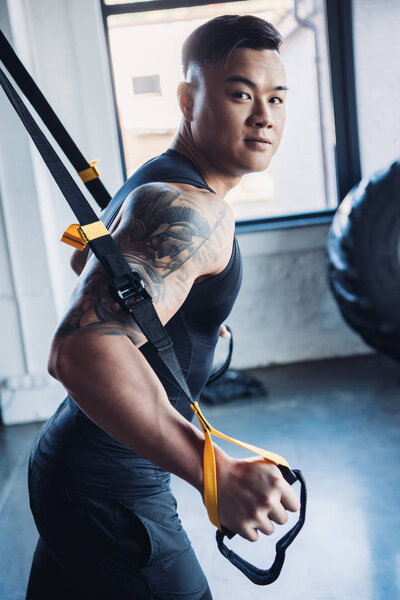 concentrated young asian muscular sportsman training with resistance bands in gym