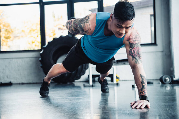 young sportsman doing one arm plank exercise at gym