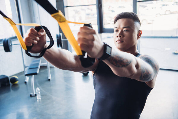 focused young muscular sportsman training with resistance bands in gym