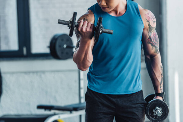 partial view of young sportsman exercising with dumbbells in gym