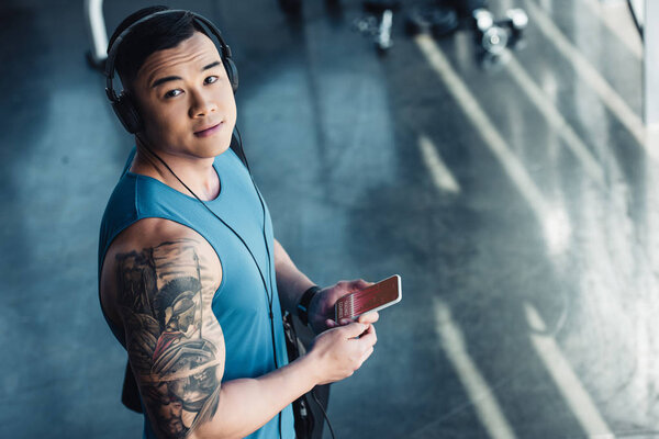 young asian sportsman using smartphone with graph on screen and listening to music 