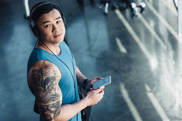 молодой азиатский спортсмен, использующий смартфон и слушающий музыку
