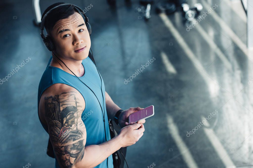 Young asian sportsman using smartphone with instagram app and listening to music