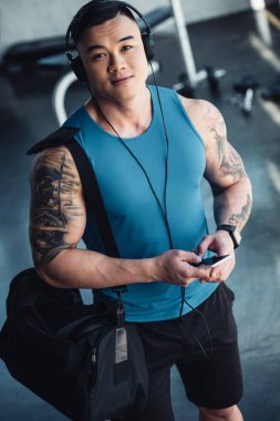 Genç Asyalı sporcu Smartphone kullanarak ve sportif çanta ile spor salonunda müzik dinlemek