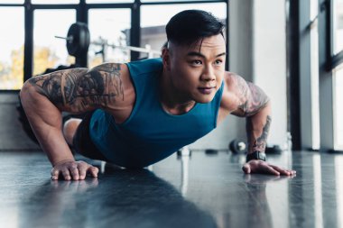 Genç Asyalı sporcu spor salonunda tahta egzersiz yaparak konsantre