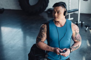 Genç Asyalı sporcu Smartphone kullanarak ve spor salonunda müzik dinlemek