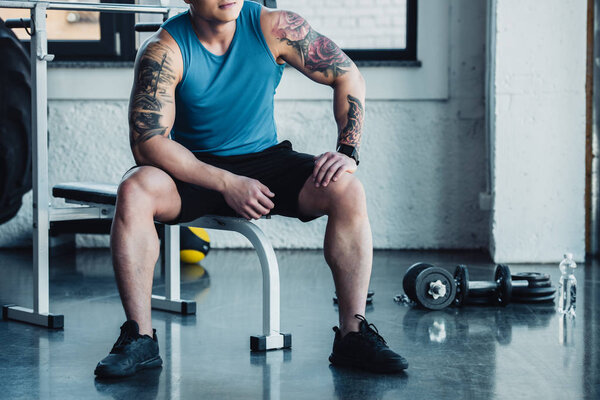 cropped view of young sportsman sitting at gym 