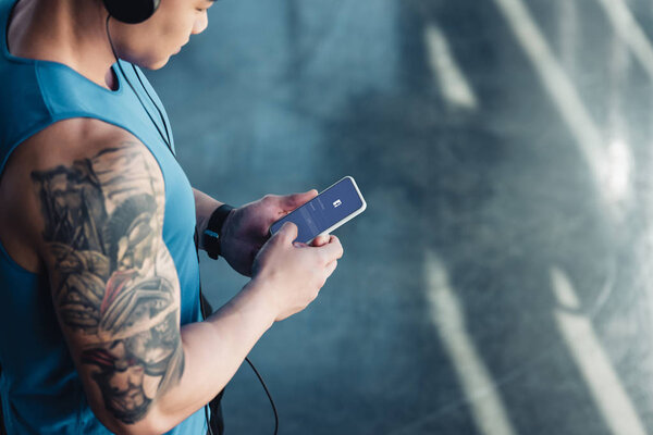 обрезанный вид молодого спортсмена с помощью смартфона с приложением facebook и прослушивания музыки
