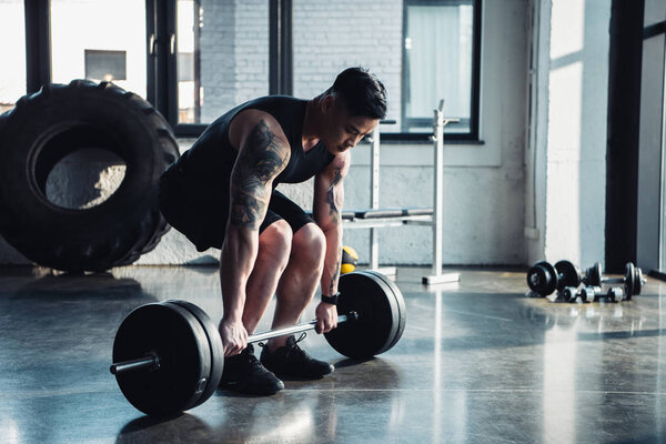 concentrated sportsman training with barbell at gym