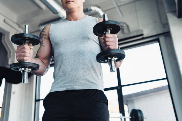 partial view of young sportsman exercising with dumbbells in gym