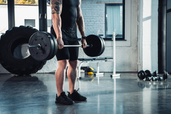 cropped view of young sportsman exercising with dumbbells in gym