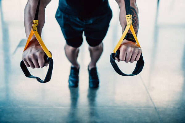 cropped view of young muscular sportsman training with resistance bands in gym