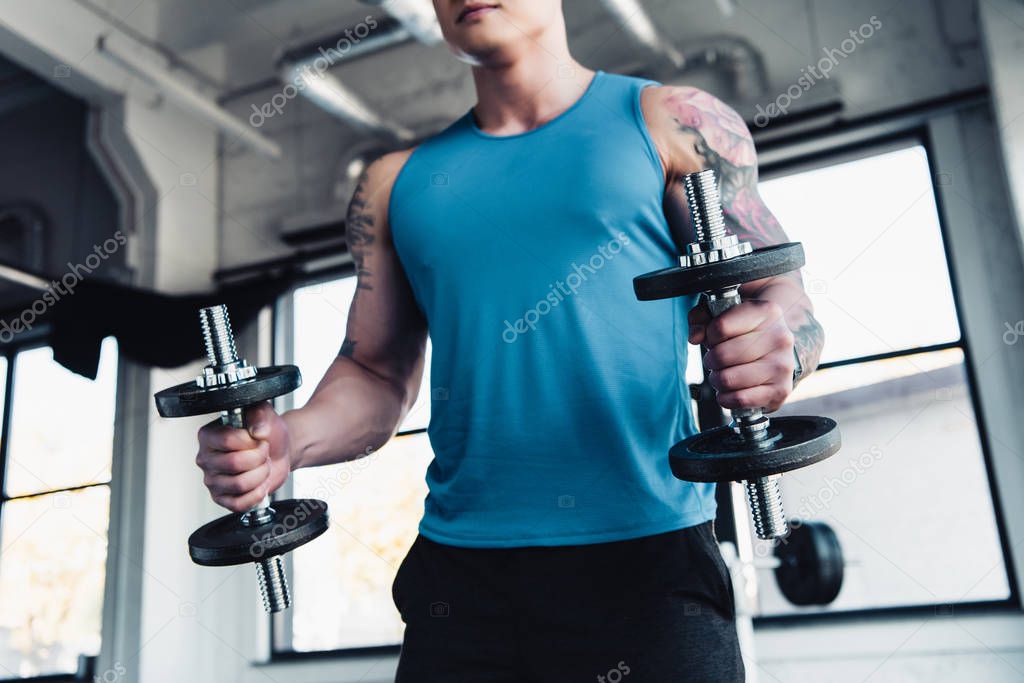 partial view of young sportsman exercising with dumbbells in gym