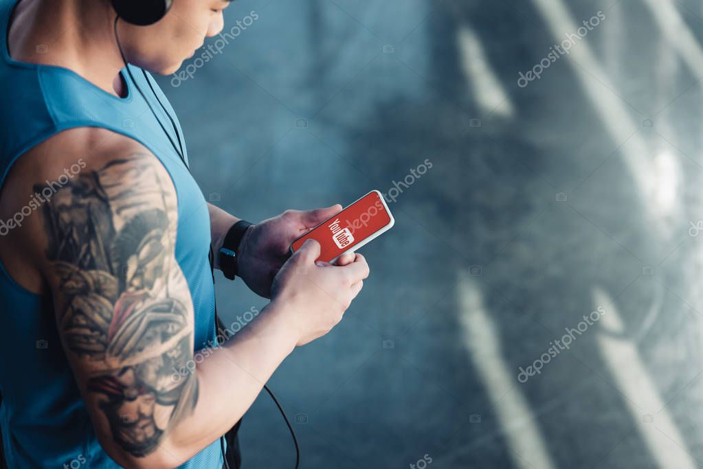 Cropped view of young sportsman using smartphone with youtube app and listening to music