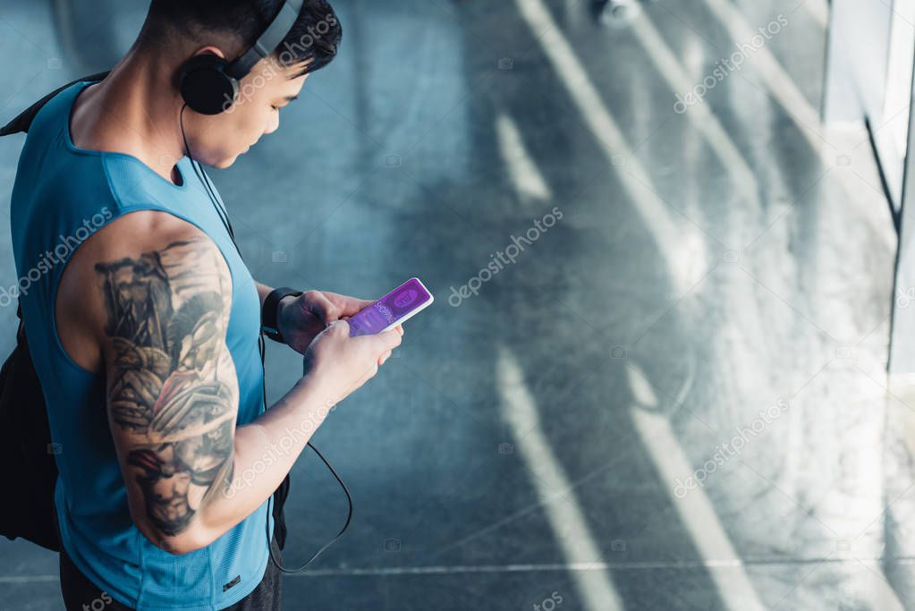 Handsome young sportsman using smartphone with shopping app and listening to music