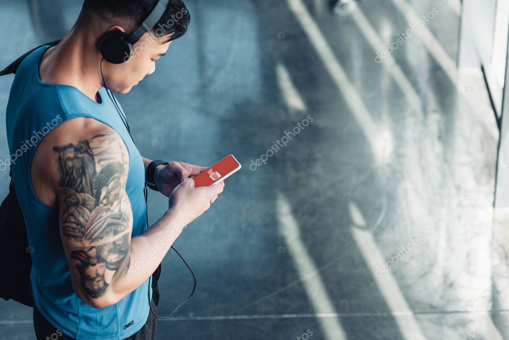 Young sportsman using smartphone with youtube app and listening to music