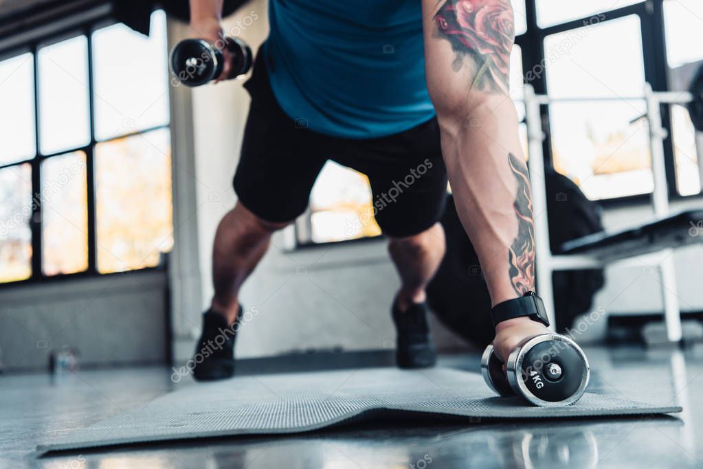 young sportsman exercising with dumbbells in gym on sport mat