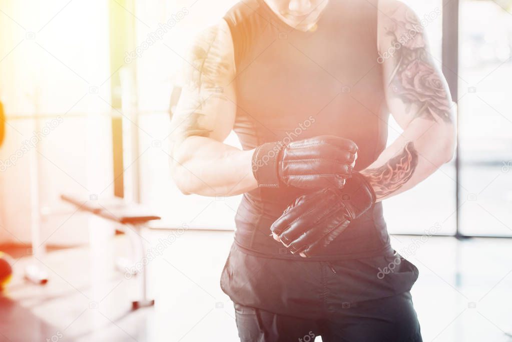 cropped view of young sportsman wearing boxing gloves in sunlight