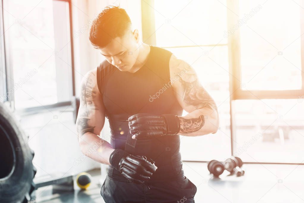 young asain sportsman wearing black boxing gloves at gym in sunlight