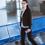 Junge schöne Geschäftsfrau in Brille, die mit Gepäck am Flughafen spazieren geht