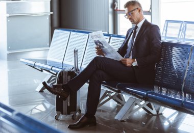 Havaalanına gidiş salonunda oturuyor ve gazete okuma yetişkin iş adamı
