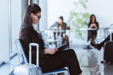 havaalanında gidiş salonunda oturan siyah klasörle yetişkin iş kadını
