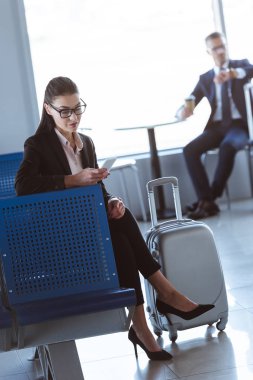 Havaalanına gitmek için smartphone ile kahve oturan işadamı iken kullanarak genç iş kadını
