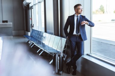 kalkış Lounge pencere yanında duran ve zaman havaalanında kontrol işadamı
