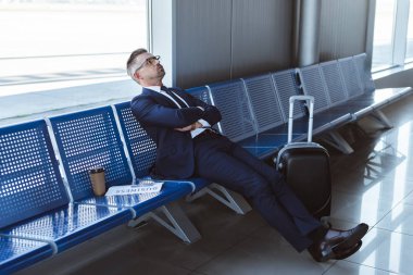 exhausted businessman in glasses sitting near window at departure lounge  clipart