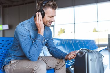 Yakışıklı adam oturmuş ve havaalanında müzik keyfi