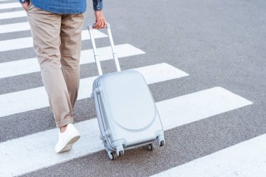 Cropped view of a tourist in white shoes pulling his luggage clipart