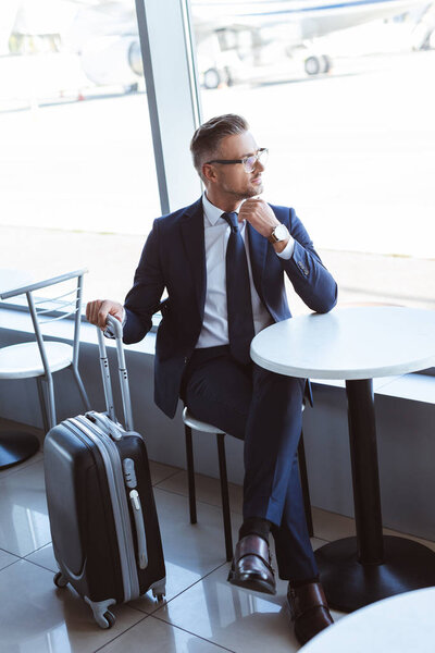 adult businessman with travel bag sitting at table in airport