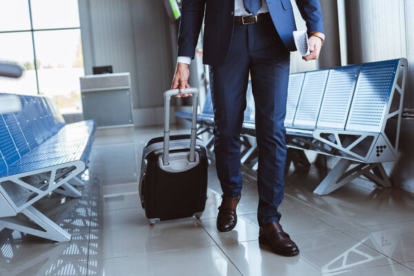 close up of businessman with luggage walking along departure lounge in airport
