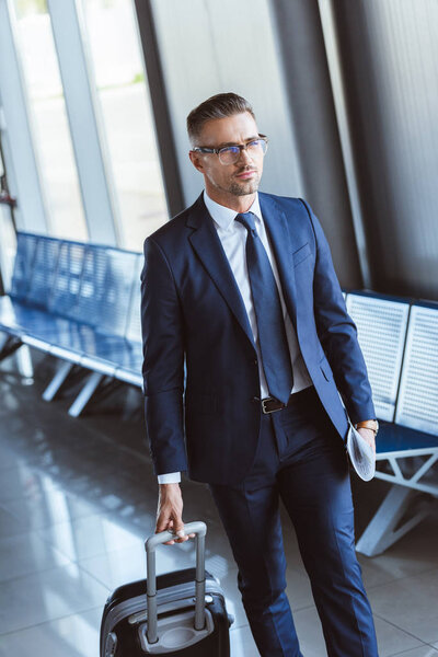 adult handsome businessman in glasses with baggage walking at airport