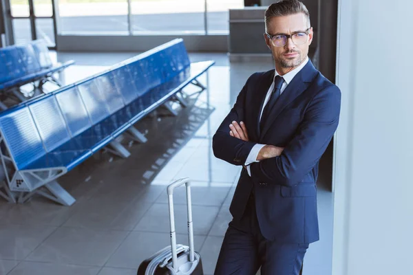 businessman in glasses standing with luggage at departure lounge in airport