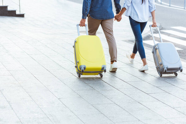 Обрезанный вид на пару туристов, держащихся за руки и вытаскивающих свой багаж