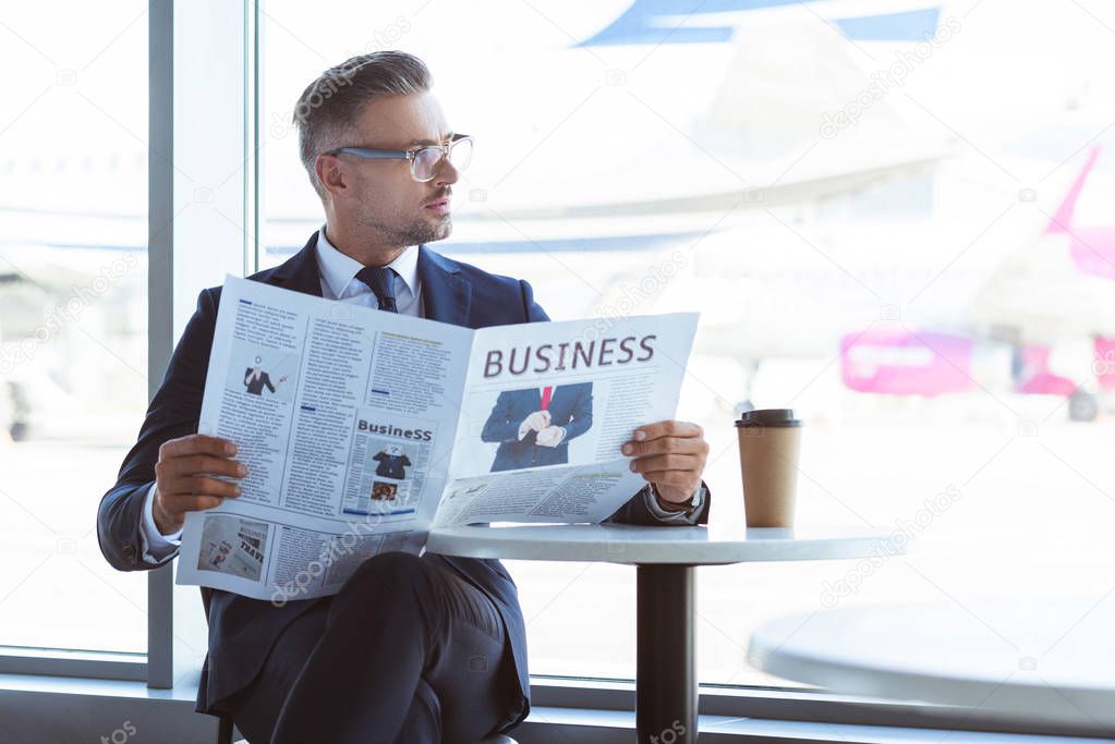 adult businessman reading newspaper and looking at window at airport