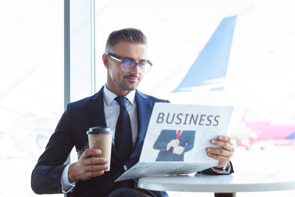 adult handsome businessman reading newspaper and holding coffee to go at airport