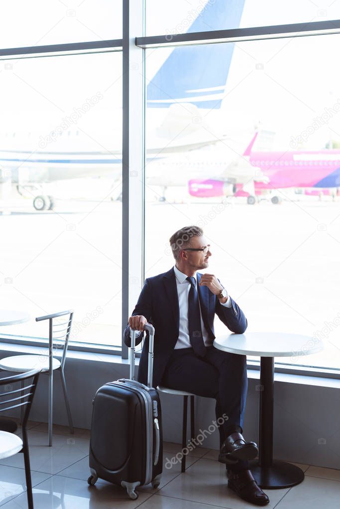 adult businessman with travel bag sitting at table in airport