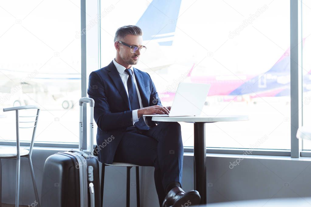 adult businessman in glasses typing on laptop at airport