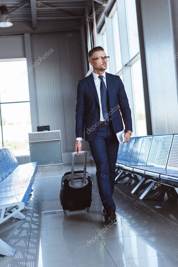 handsome businessman in glasses walking along departure lounge in airport